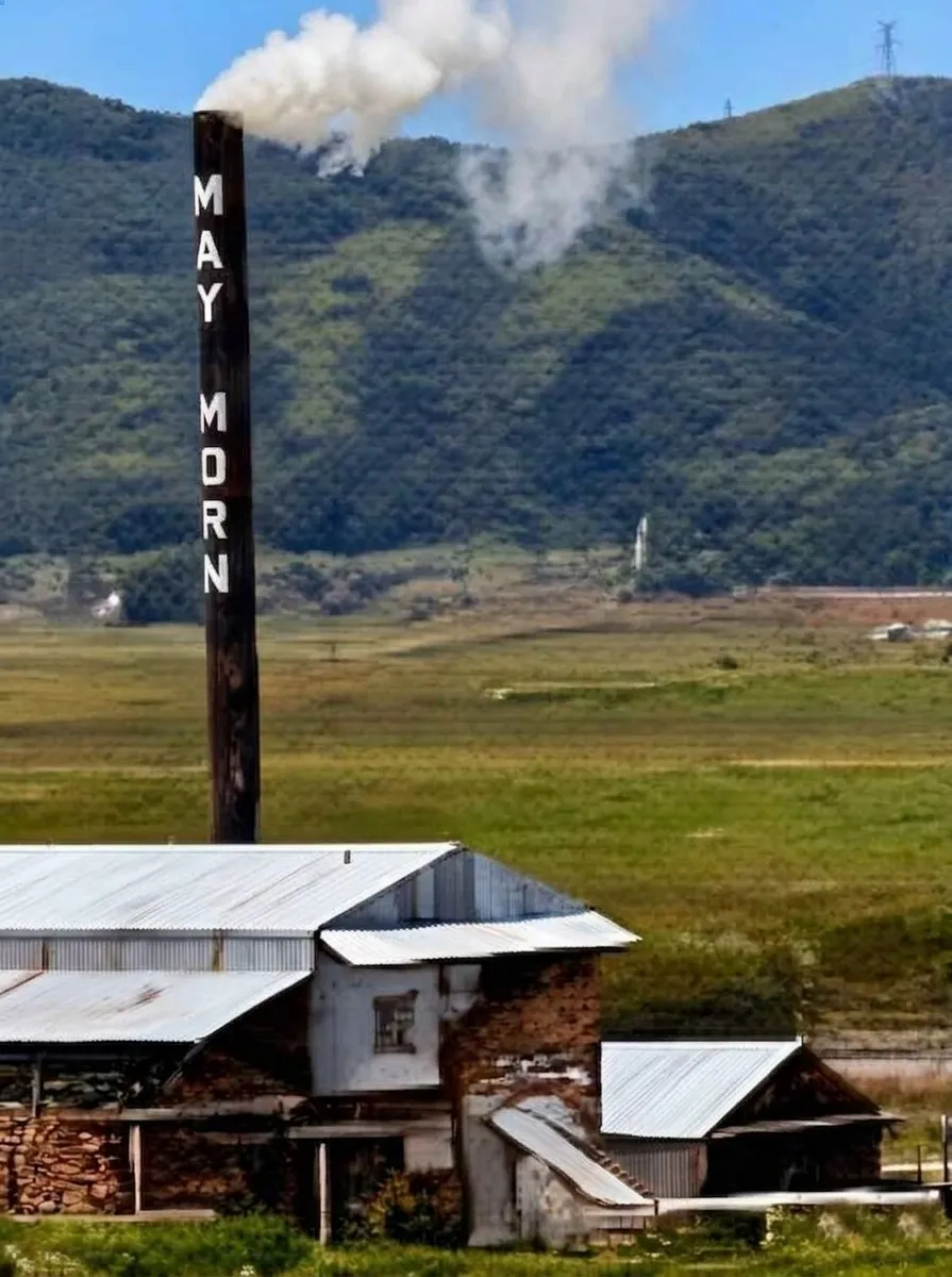 The May Morn sawmill chimney, smoke rising from it, above the mill buildings and the valley beyond